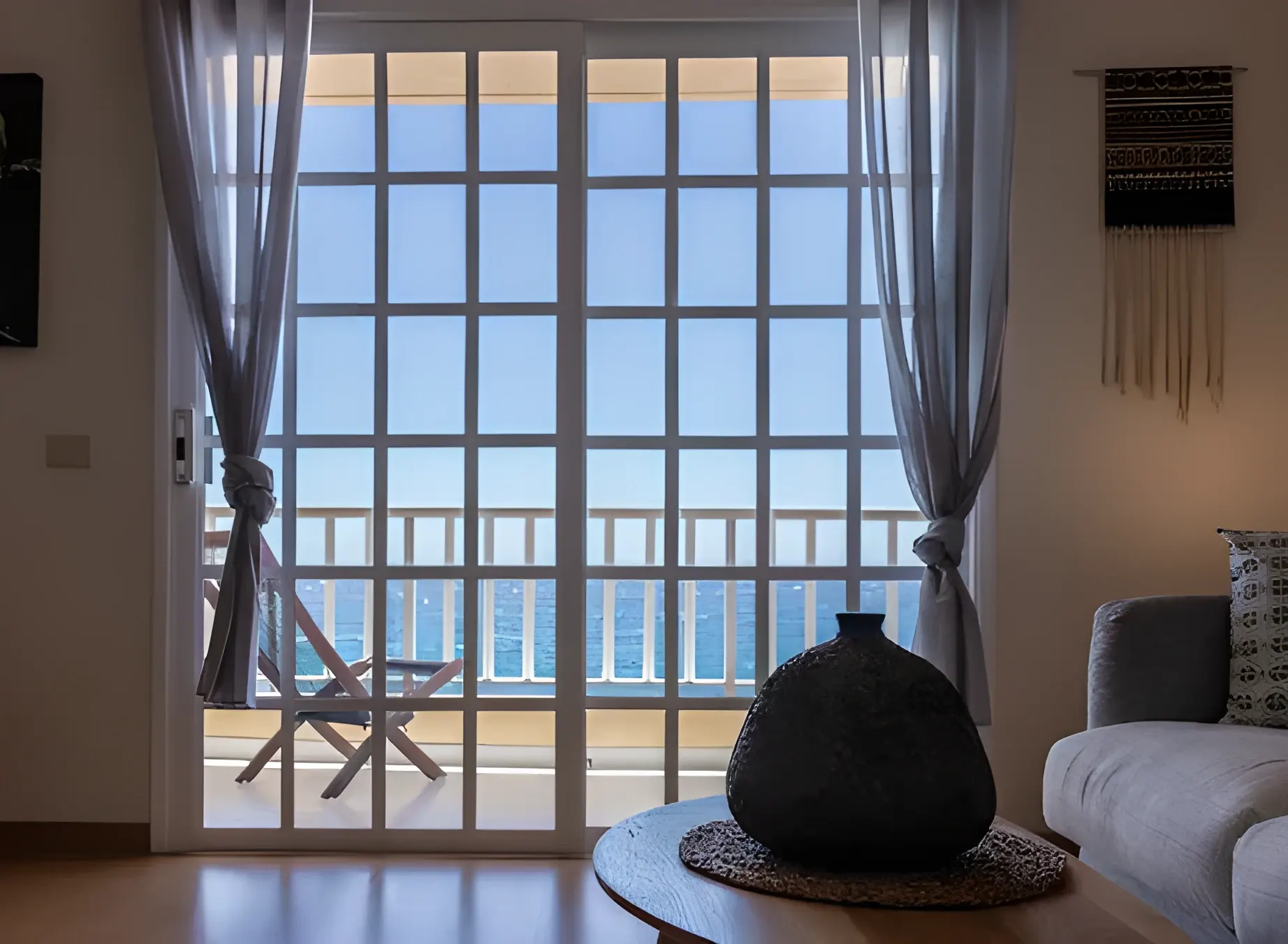 Ventanal del salón con vistas al mar y silla de terraza al otro lado